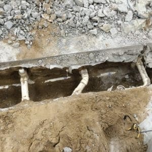 Image of exposed concrete foundation showing drain and waste piping in the ground.