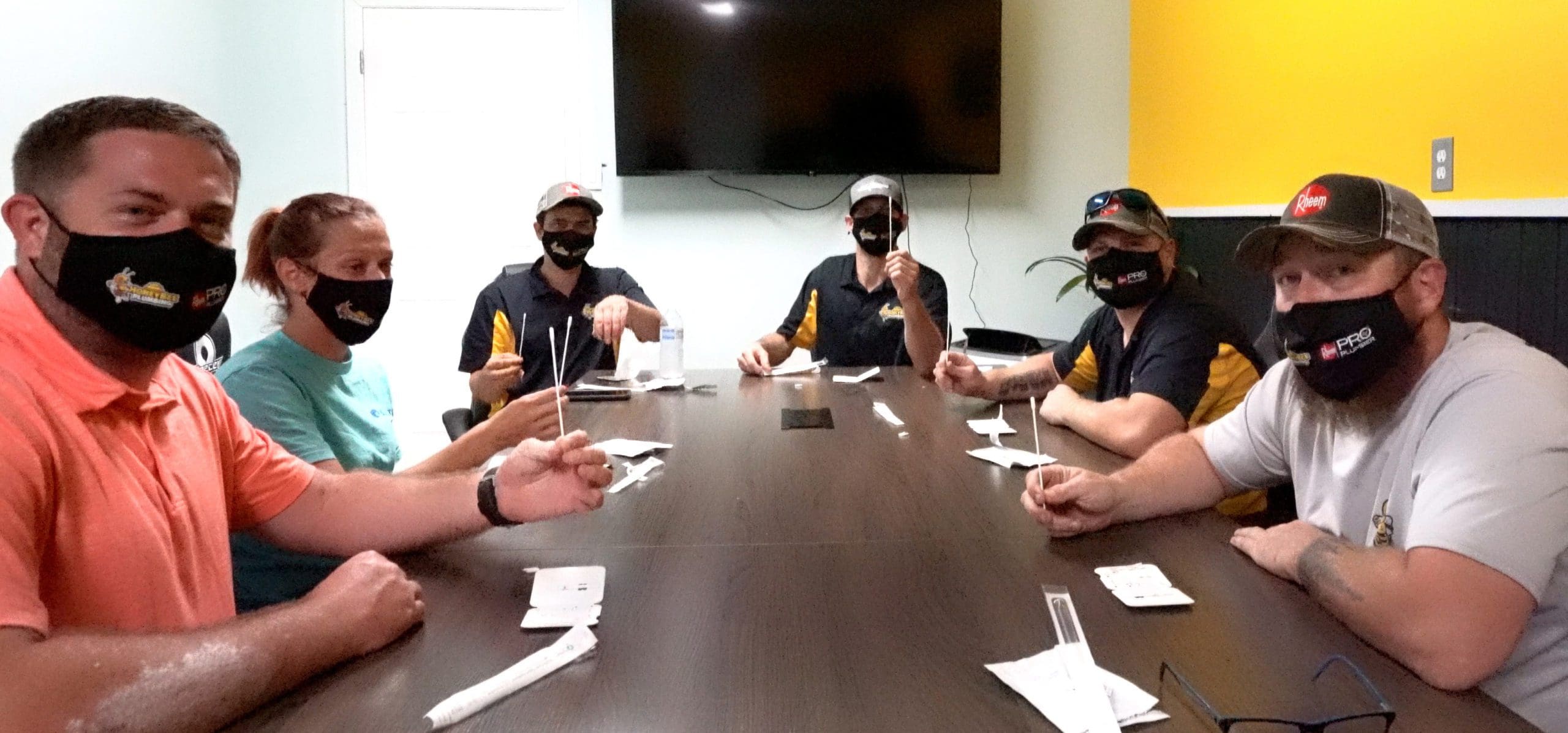 Honey Bee Plumbing team members sitting at a conference table, performing COVID-19 testing before starting their workday