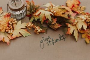 Autumnal image featuring the phrase "Give Thanks," surrounded by leaves and a glowing candle