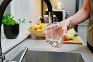 Woman pouring water into a glass from a kitchen faucet