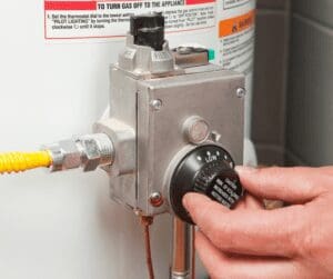 Hand adjusting temperature dial on a gas water heater