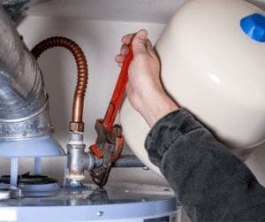 Person using a pipe wrench to tighten a pipe on a water heater