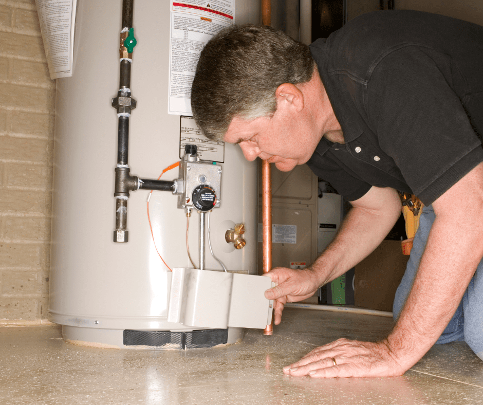 An older gentleman kneeling and removing the burner cover from a gas tank water heater.