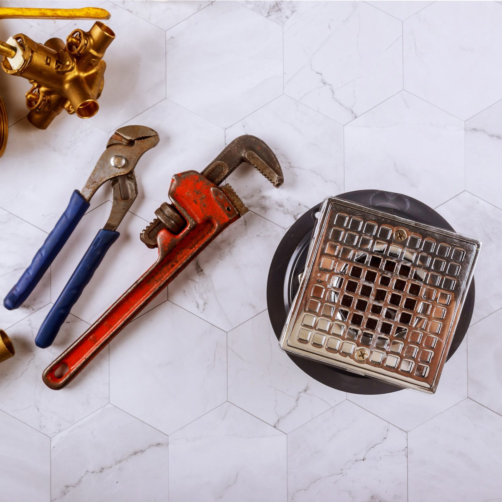 Shower drain surrounded by various plumbing parts and tools