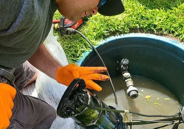 Plumber kneeling by a lift station reservoir, working on a grinder pump