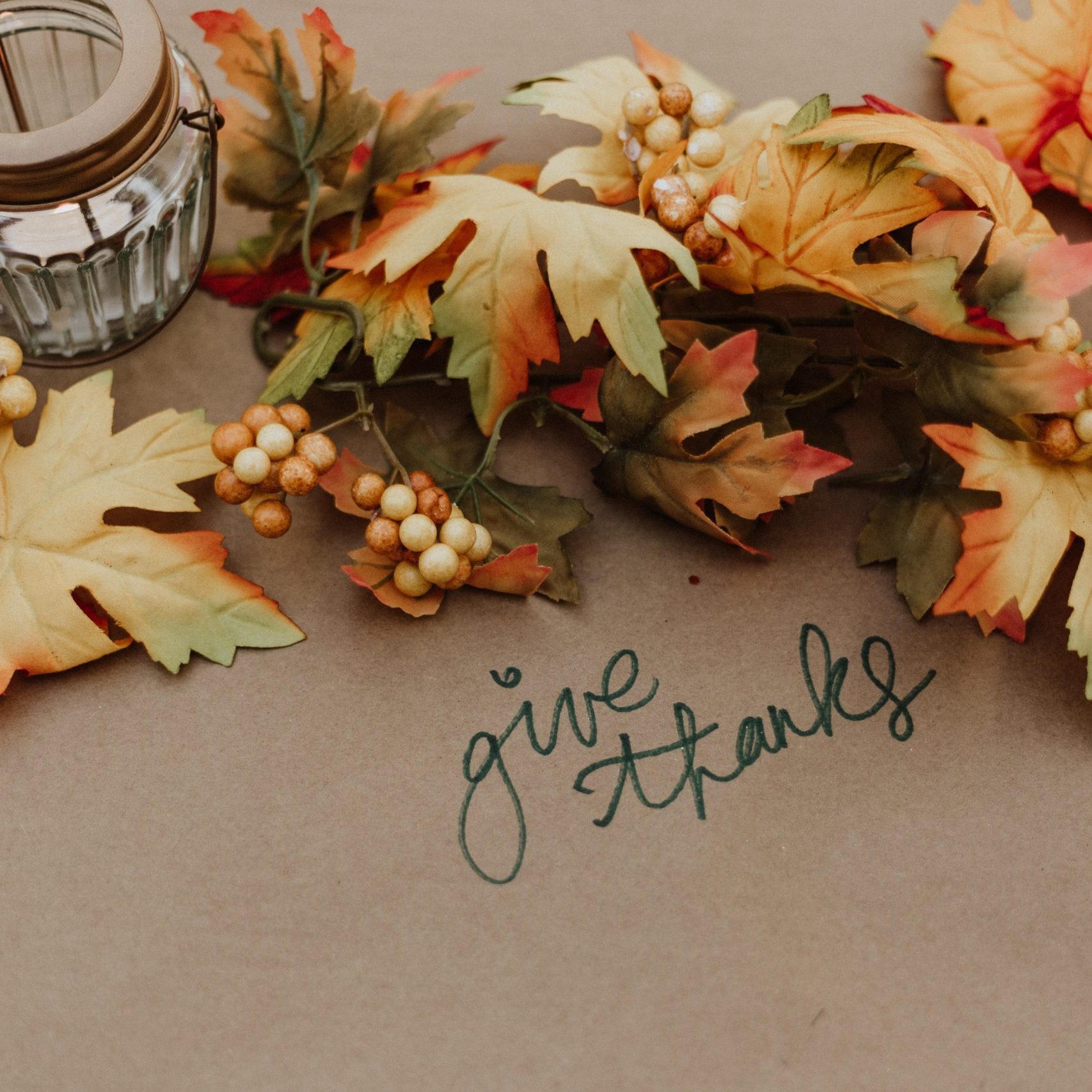 Autumnal image featuring the phrase "Give Thanks," surrounded by leaves and a glowing candle